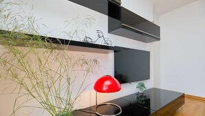 A modern living room with a black entertainment unit, a red floor lamp, and a wall-mounted TV. - Vista Del Mare (Dubrovnik)