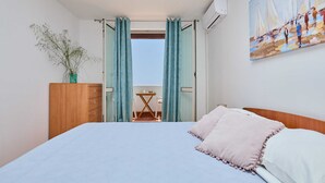 A bedroom with a bed, a wooden dresser, a potted plant, a painting, and a balcony with a table and chairs. - Vista Del Mare (Dubrovnik)