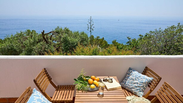 A wooden table with a fruit bowl, glasses, and a book, set against a scenic ocean view. - Vista Del Mare (Dubrovnik)