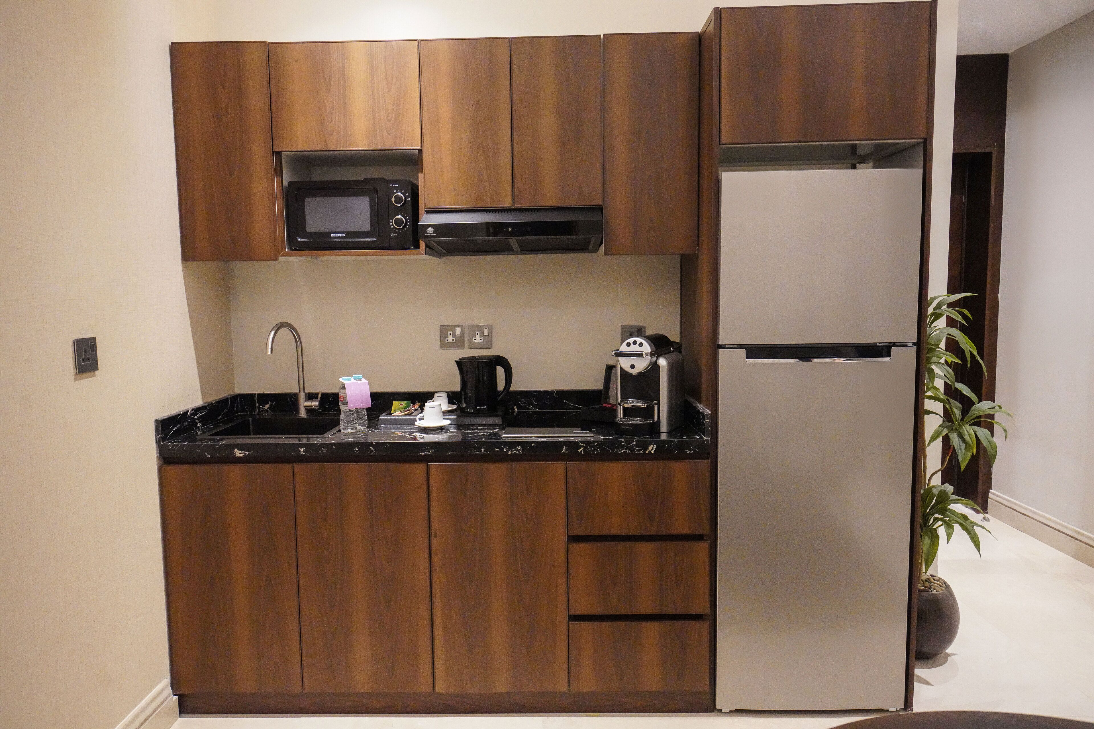 A compact kitchen with wooden cabinets, a microwave, a coffee maker, and a refrigerator.