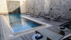 Zona de piscina con una pileta rectangular, sillones de descanso y una pequeña mesa.