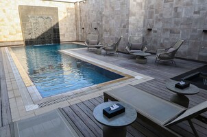 A poolside area with a rectangular pool, lounge chairs, and a small table.
