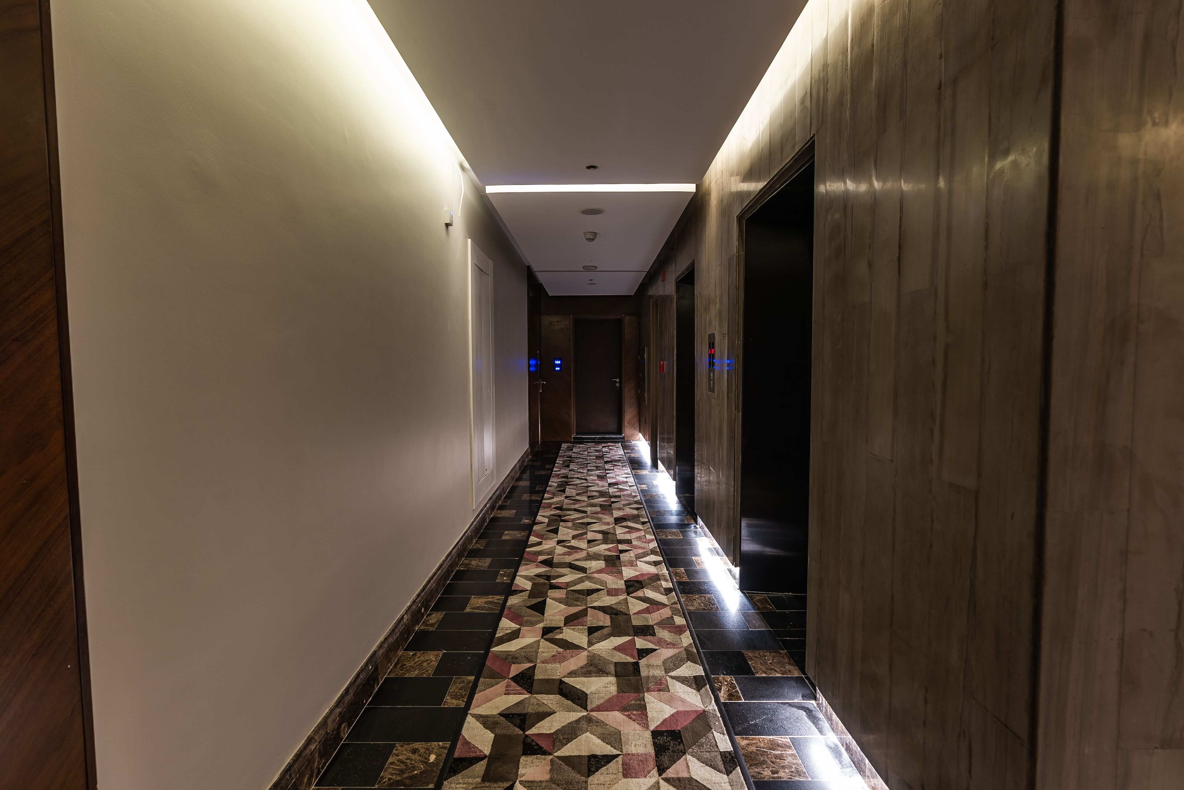 A hallway with a patterned floor, wooden walls, and a ceiling with recessed lighting.