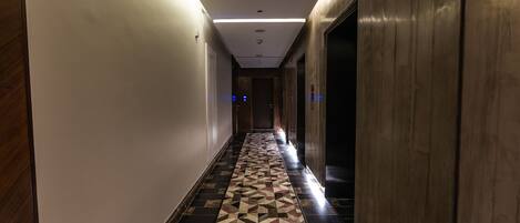 A hallway with a patterned floor, wooden walls, and a ceiling with recessed lighting.