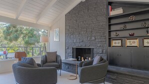 Un salon moderne avec une cheminée en pierre, des fauteuils à revêtement gris et une bibliothèque agrémentée d’objets décoratifs.