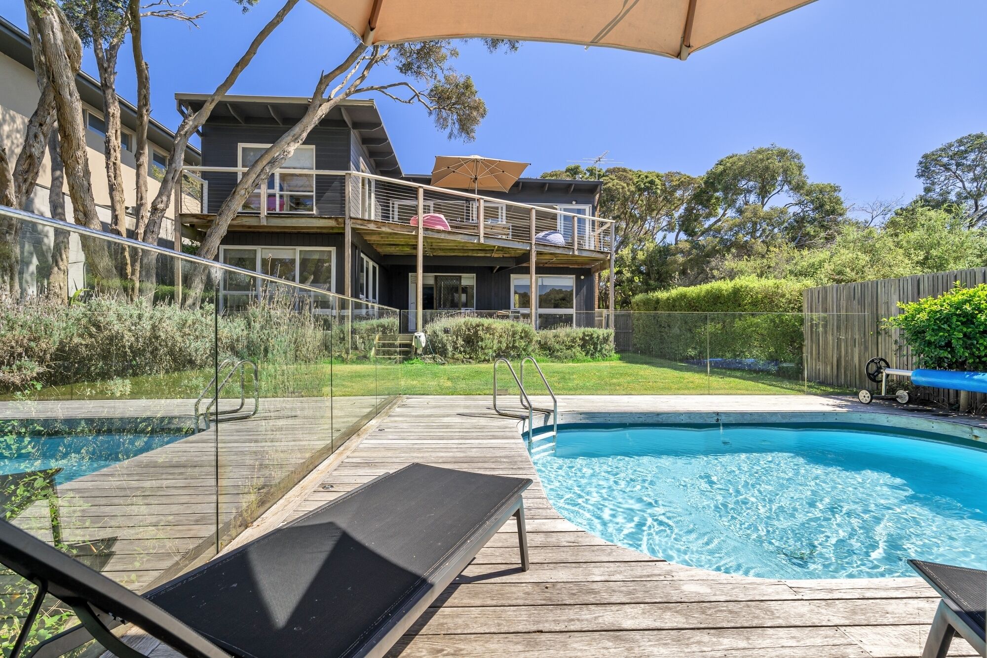 A backyard with a swimming pool, wooden deck, and a house with a balcony.