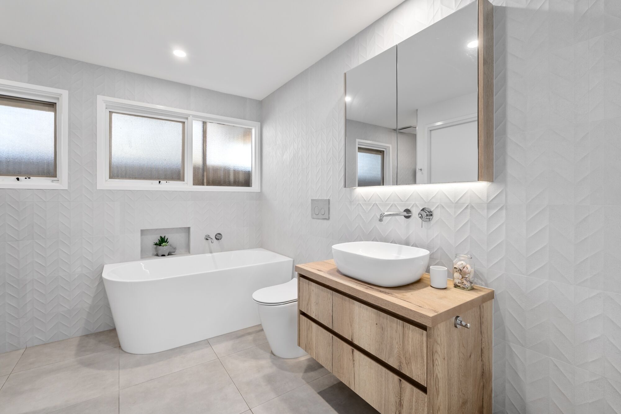 A modern bathroom with a freestanding bathtub, a toilet, and a vanity with a large mirror.