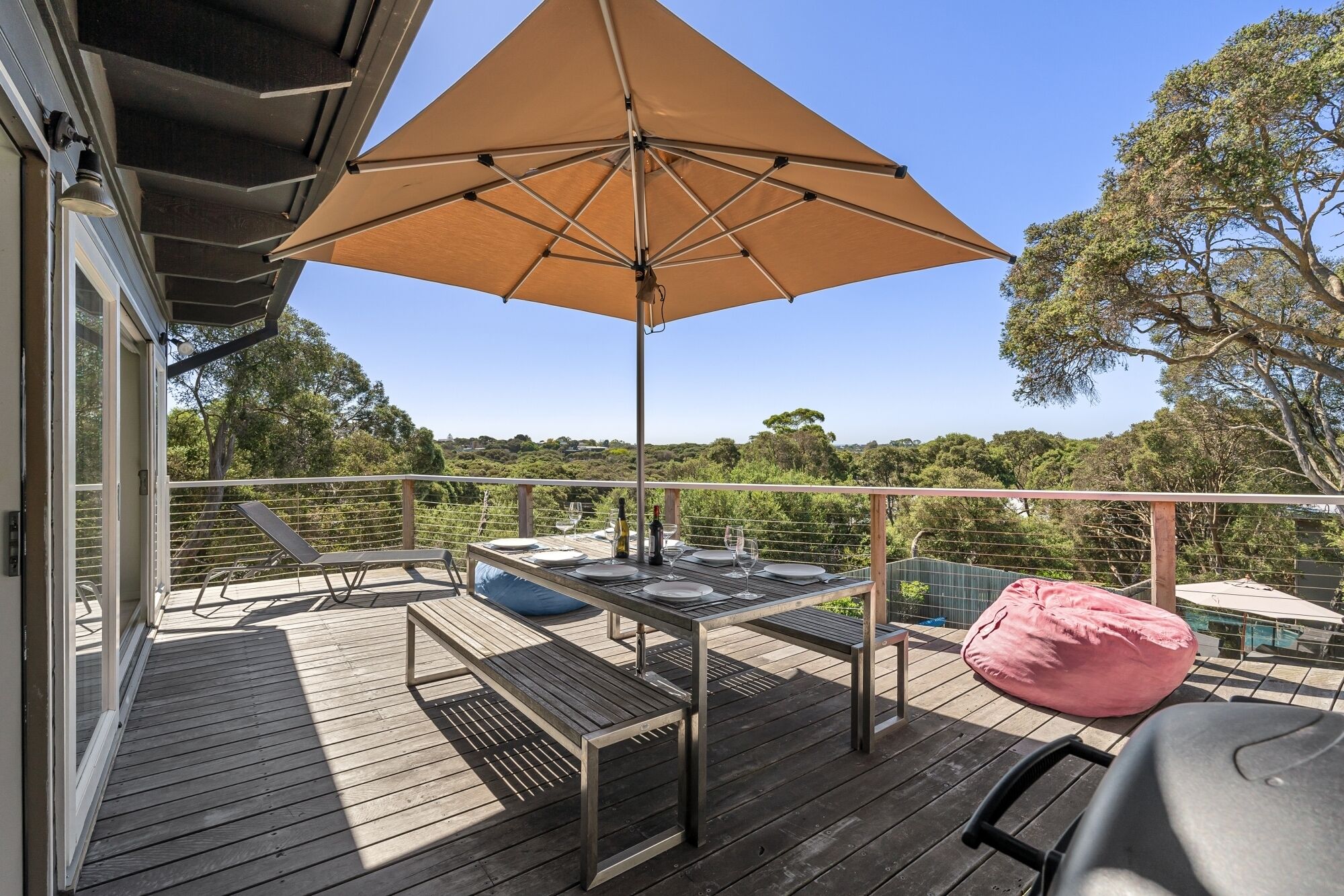 A wooden deck with a table and chairs, a large umbrella, and a pink bean bag.