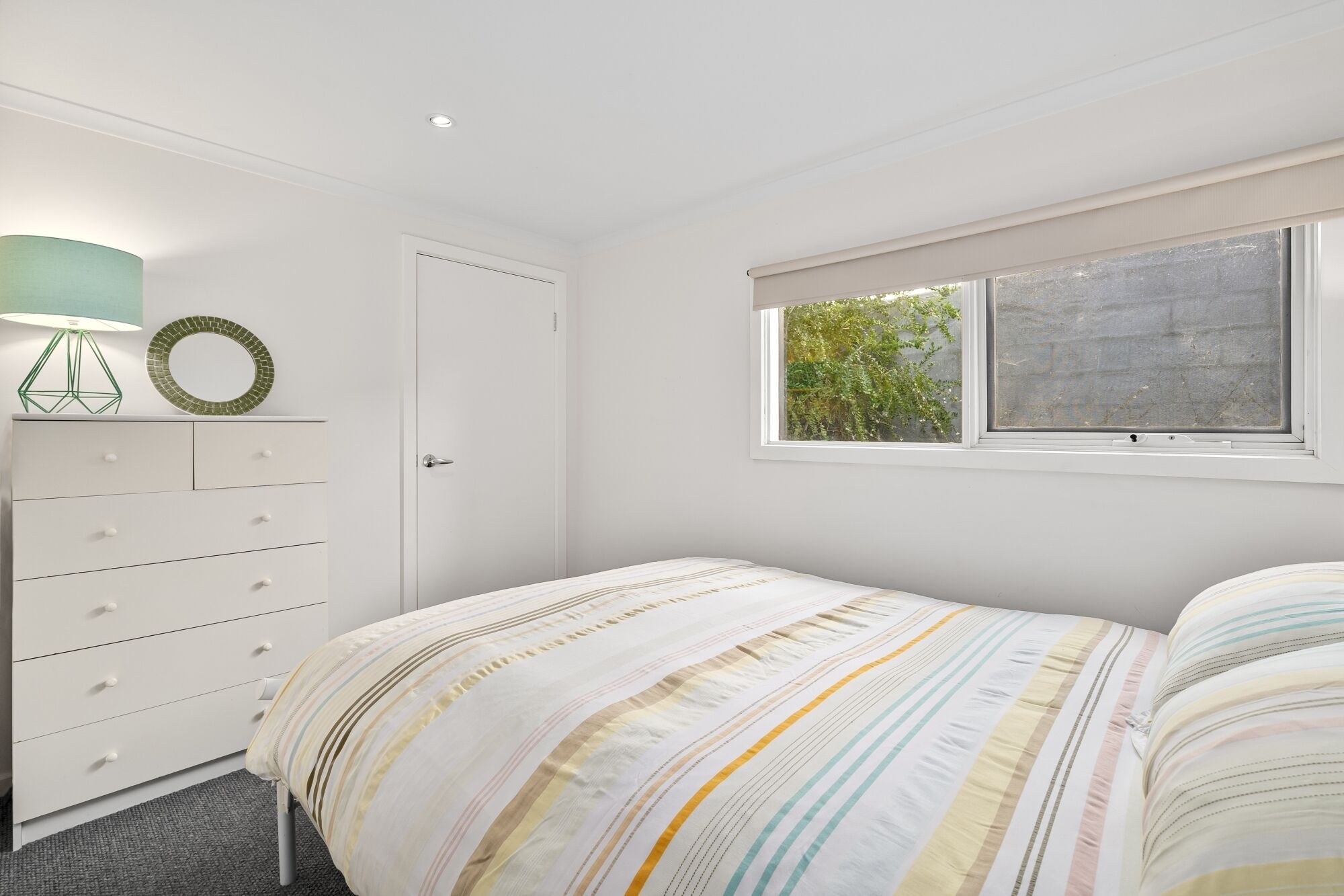Une chambre à coucher avec un lit, une commode, une lampe et une fenêtre donnant sur un paysage verdoyant.