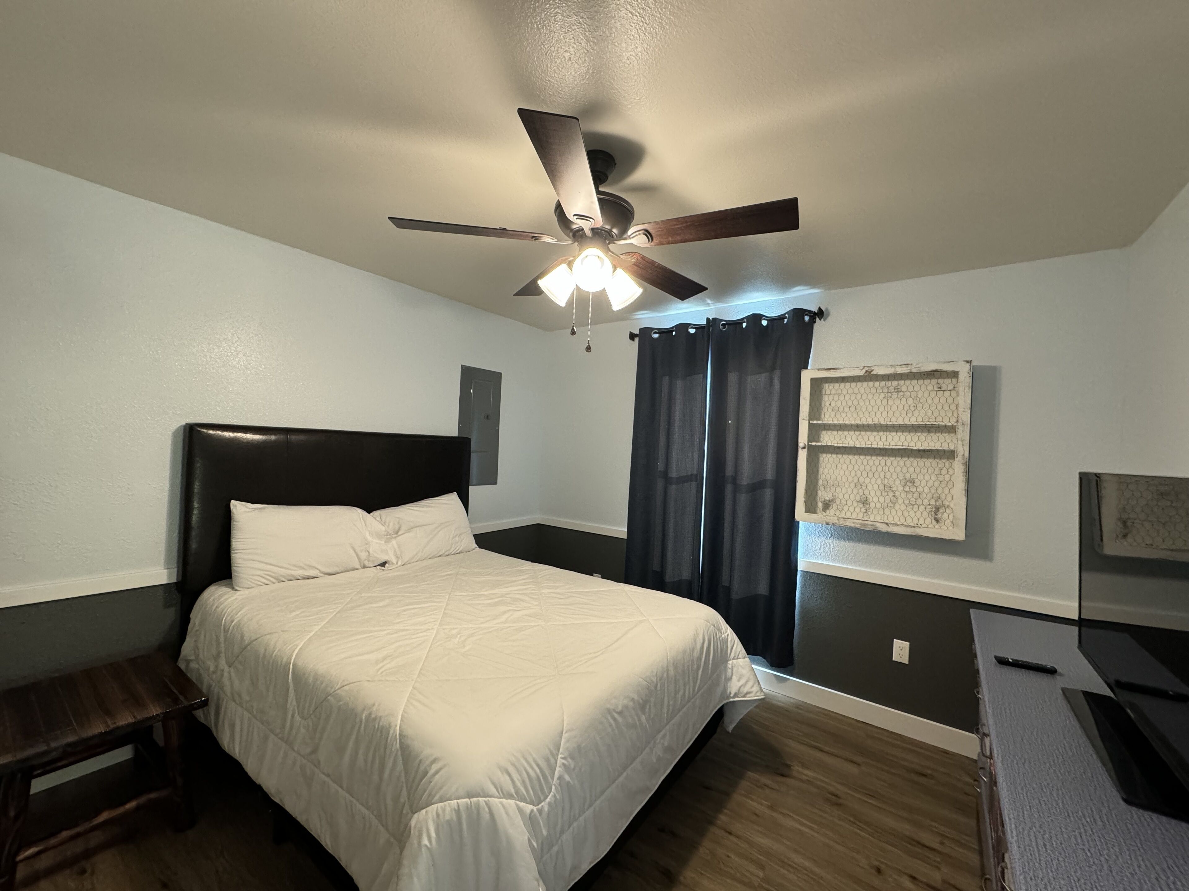 A bedroom with a bed, a ceiling fan, a nightstand, a dresser, and a window with curtains.
