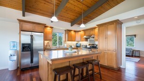 Una cocina moderna con armarios de madera, un refrigerador de acero inoxidable, una isla grande con taburetes y un dispensador de agua.