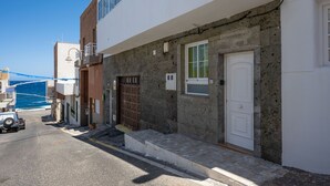 Una calle estrecha con un edificio blanco de fachada de piedra, puerta de madera y un escalón que lleva a la entrada.