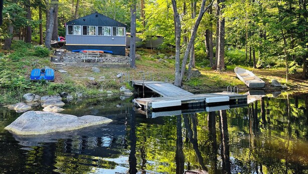 Una cabaña con un muelle que se adentra en un lago tranquilo, rodeada de un bosque denso.