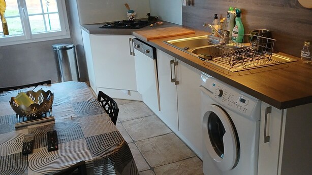 A compact kitchen with a built-in washing machine, a sink, and a dining area with a table and chairs.