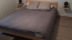A bedroom with a bed, two bedside tables, a wall-mounted lamp, and a framed picture above the bed.