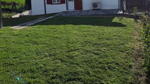 A small white building with a red-tiled roof, a single door, and a small air conditioning unit in front.