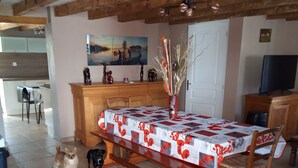 A dining area with a wooden table and chairs, a vase with dried plants, and a painting on the wall.