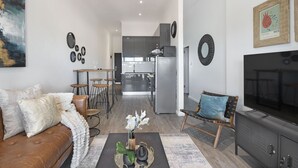 A modern living room with a sofa, coffee table, and decorative items. A kitchen is visible in the background with a refrigerator and cabinets. - Atlantic Port 9 (Cape Town)