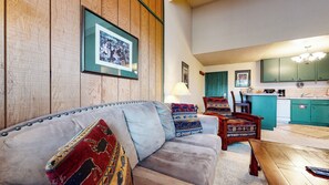 A cozy living room with a sofa, chairs, and a coffee table. There is a framed picture on the wall and a lamp on a side table.