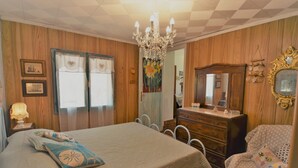 A bedroom with a bed, dresser, chair, and chandelier. - La Rotta by Solturelba (Capoliveri)