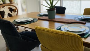 Un comedor con una mesa de madera dispuesta para dos personas, una planta en maceta y una silla con estampado de vaca.