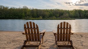 Two wooden Adirondack chairs facing a lake with a forested shoreline. - Family-Friendly Cozy Cabin Hot Tub, Fire Pit, Outdoor Pool & Ping Pong table (Clifton township)