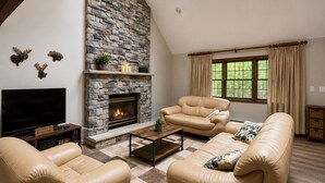 A living room with a stone fireplace, leather sofas, a coffee table, and a television. - Family-Friendly Cozy Cabin Hot Tub, Fire Pit, Outdoor Pool & Ping Pong table (Clifton township)