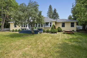 A two-story house with a front porch, a small front yard, and a picnic table. - Charming Burt Lake Cottage (Cheboygan)