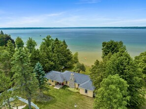 A house with a stone chimney, a porch, and a view of a lake. - Charming Burt Lake Cottage (Cheboygan)