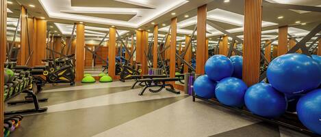 Une salle de sport équipée de matériel d’exercice, avec des piliers en bois et des ballons d’exercice bleus.