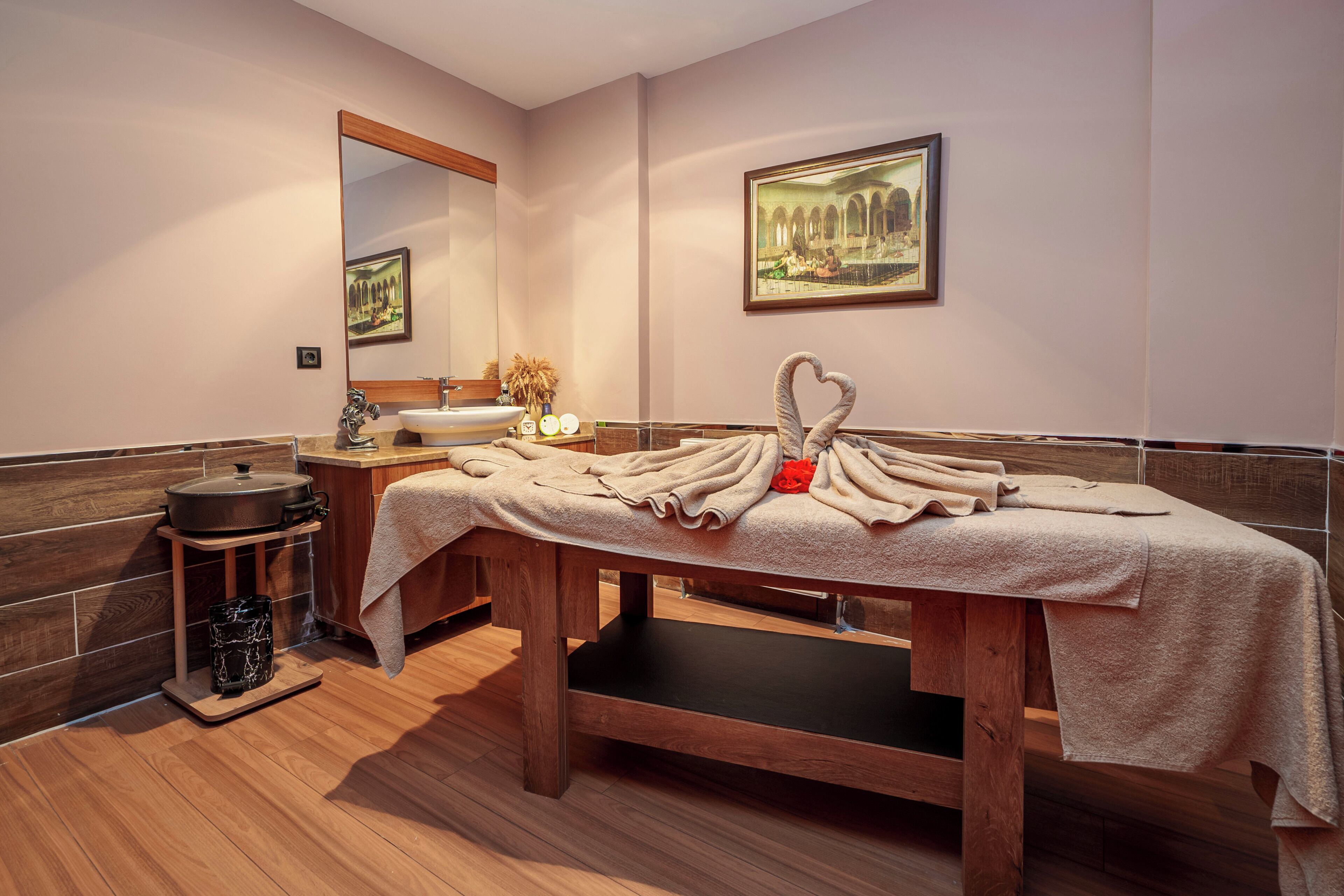 A spa room with a wooden bench, a sink, a mirror, and a framed picture on the wall.