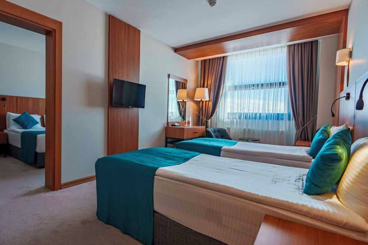 Quarto de hotel com duas camas, televisão, escrivaninha e janela com cortinas.