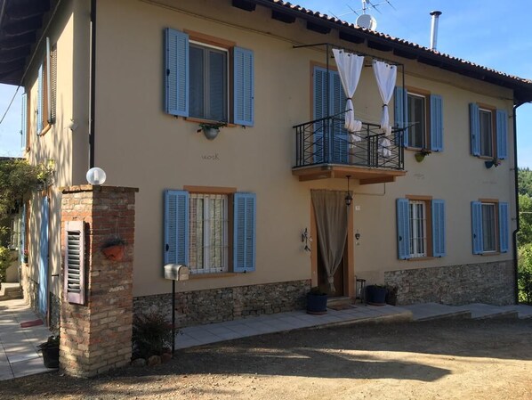 Une maison à deux étages dotée d’un balcon, de volets et d’un petit porche à l’avant.