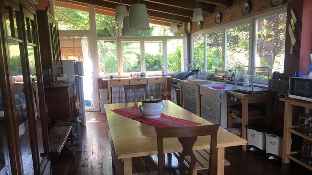 Een gezellige keuken met houten meubels, een eettafel en grote ramen met uitzicht op de natuur.