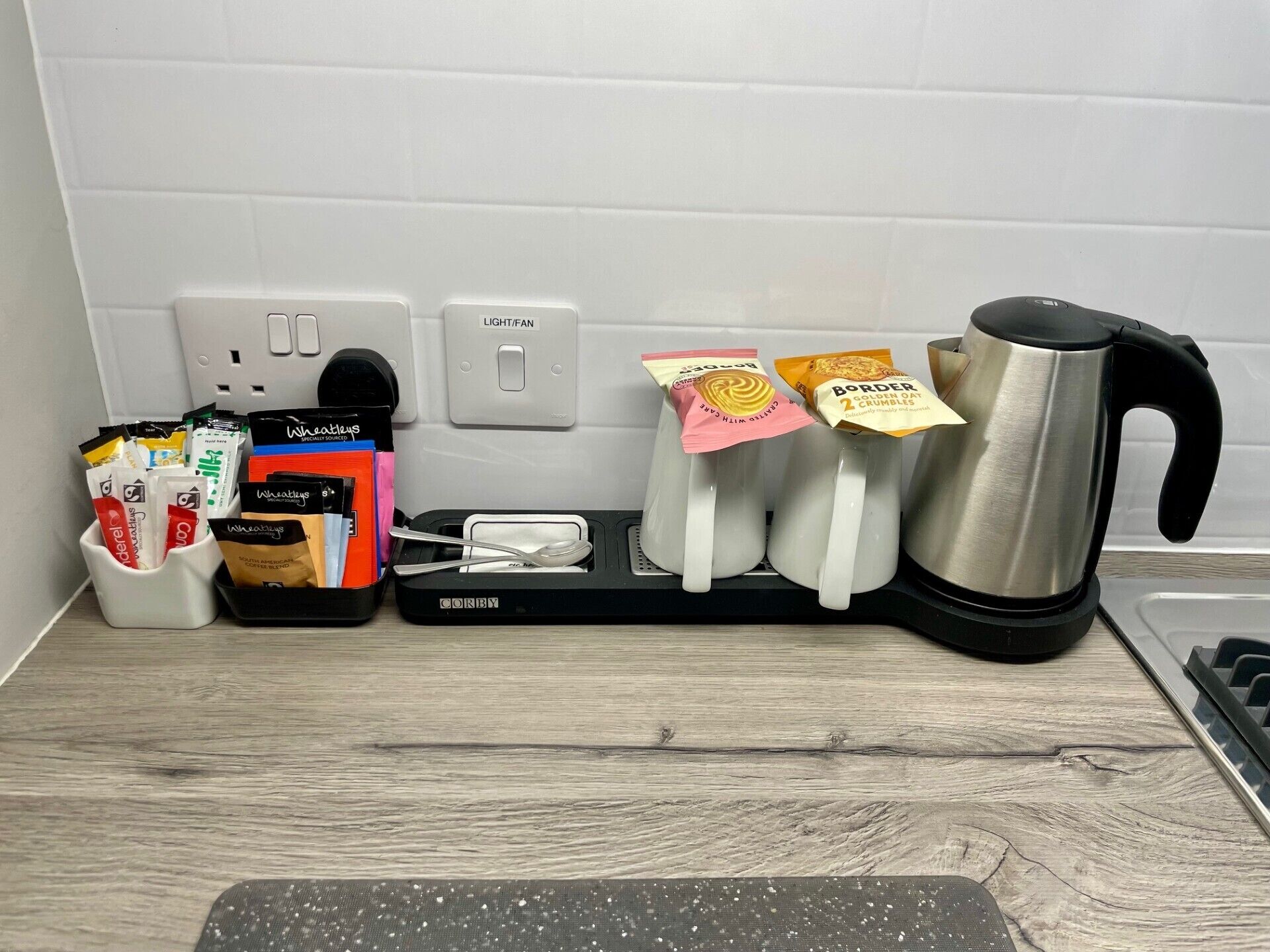 A kitchen counter with a coffee maker, a kettle, a toaster, and a tray with coffee pods and a spoon.