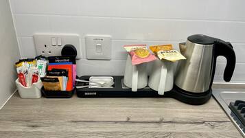 A kitchen counter with a coffee maker, a kettle, a toaster, and a tray with coffee pods and a spoon.