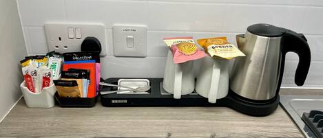 A kitchen counter with a coffee maker, a kettle, a toaster, and a tray with coffee pods and a spoon.