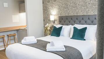 A hotel room with a large bed, two white towels, a grey headboard, and a patterned wallpaper.