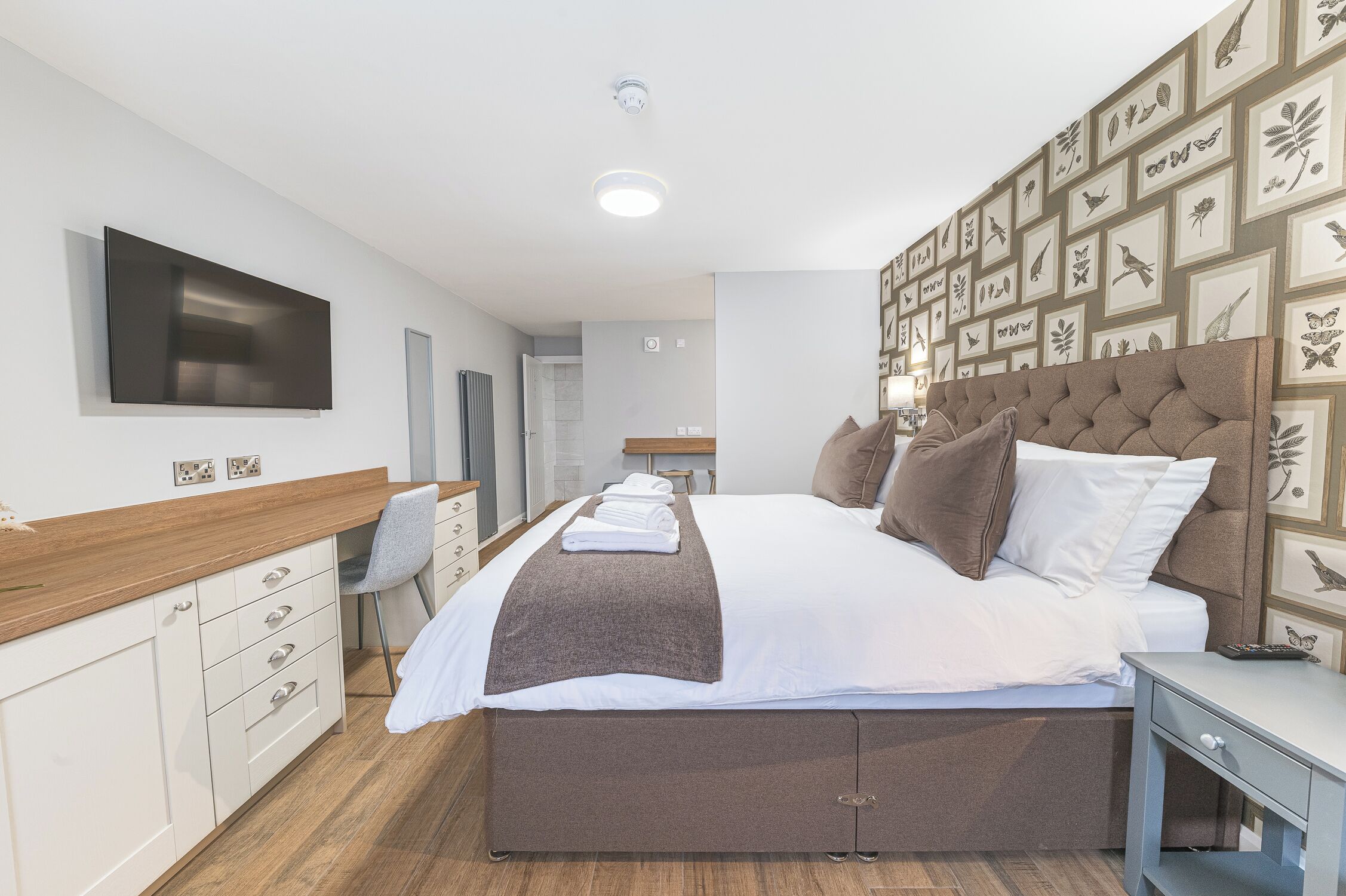Una habitación de hotel moderna con una cama grande, un televisor de pantalla plana montado en la pared, un aparador de madera y un muro decorado con fotografías enmarcadas.