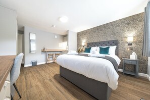 A modern hotel room with a large bed, a desk, and a kitchenette.