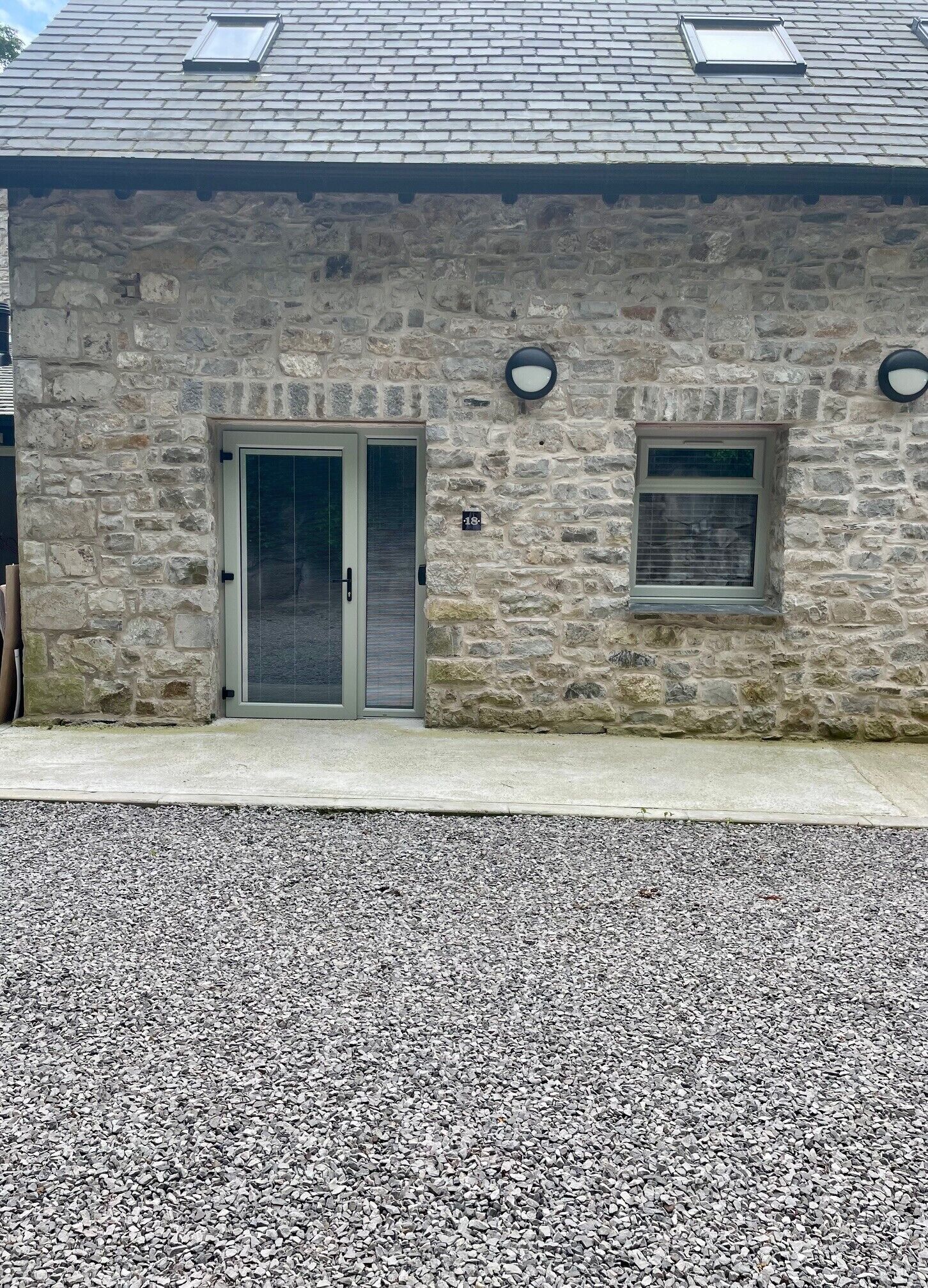 Un edificio de piedra con un camino de grava, una puerta con reja metálica y dos ventanas pequeñas.