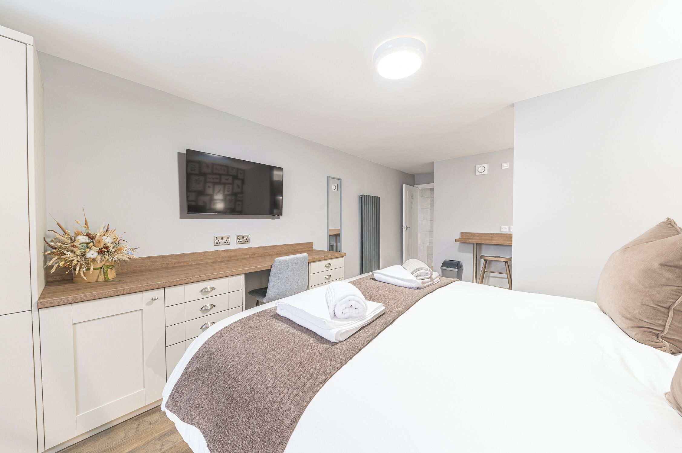 Une chambre d’hôtel moderne équipée d’un lit, d’un bureau, d’une chaise et d’un téléviseur fixé au mur.