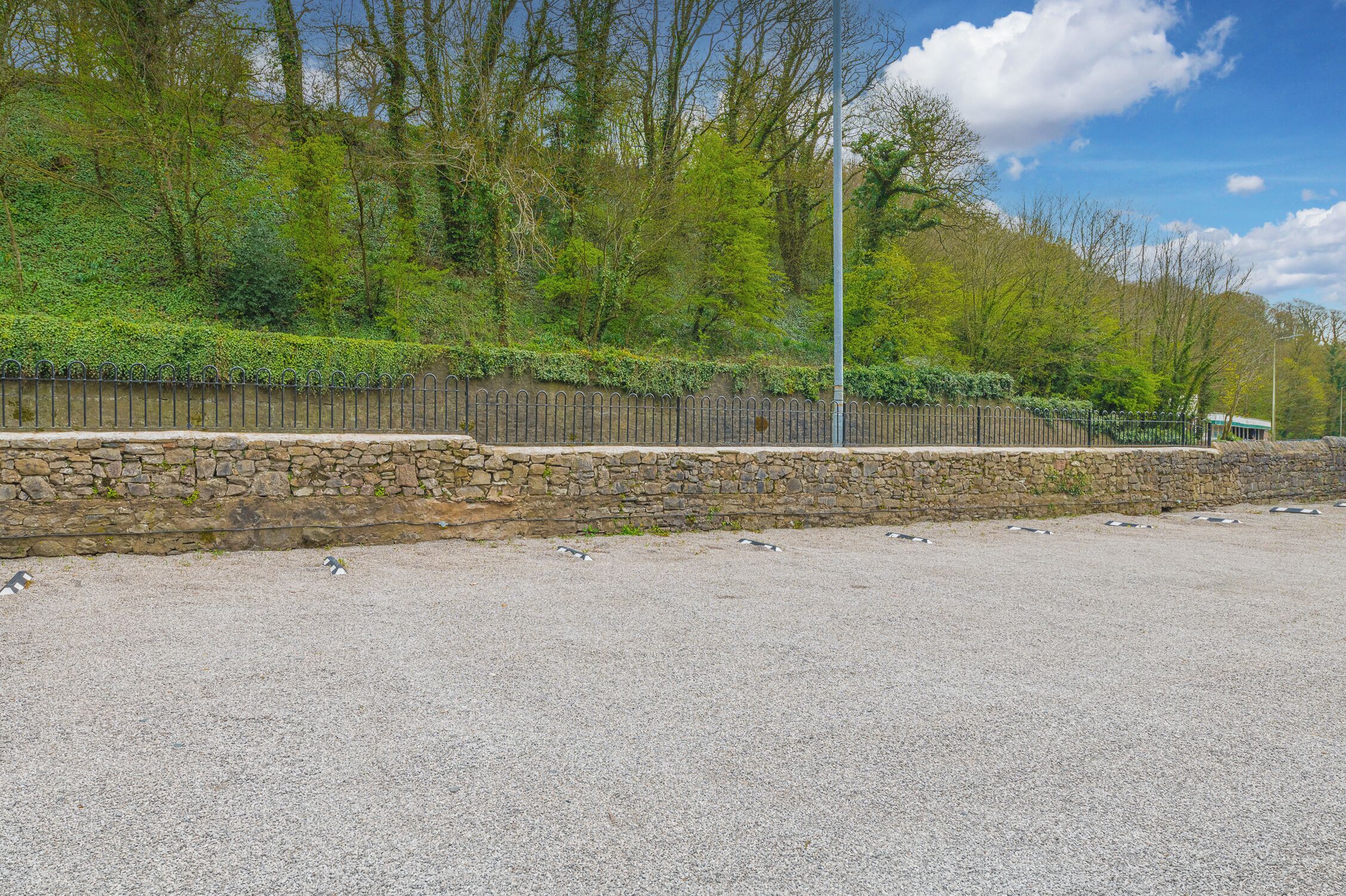 A gravel area with a stone wall and a metal fence.