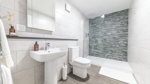 Un baño moderno con lavamanos, inodoro y zona de ducha blancos.