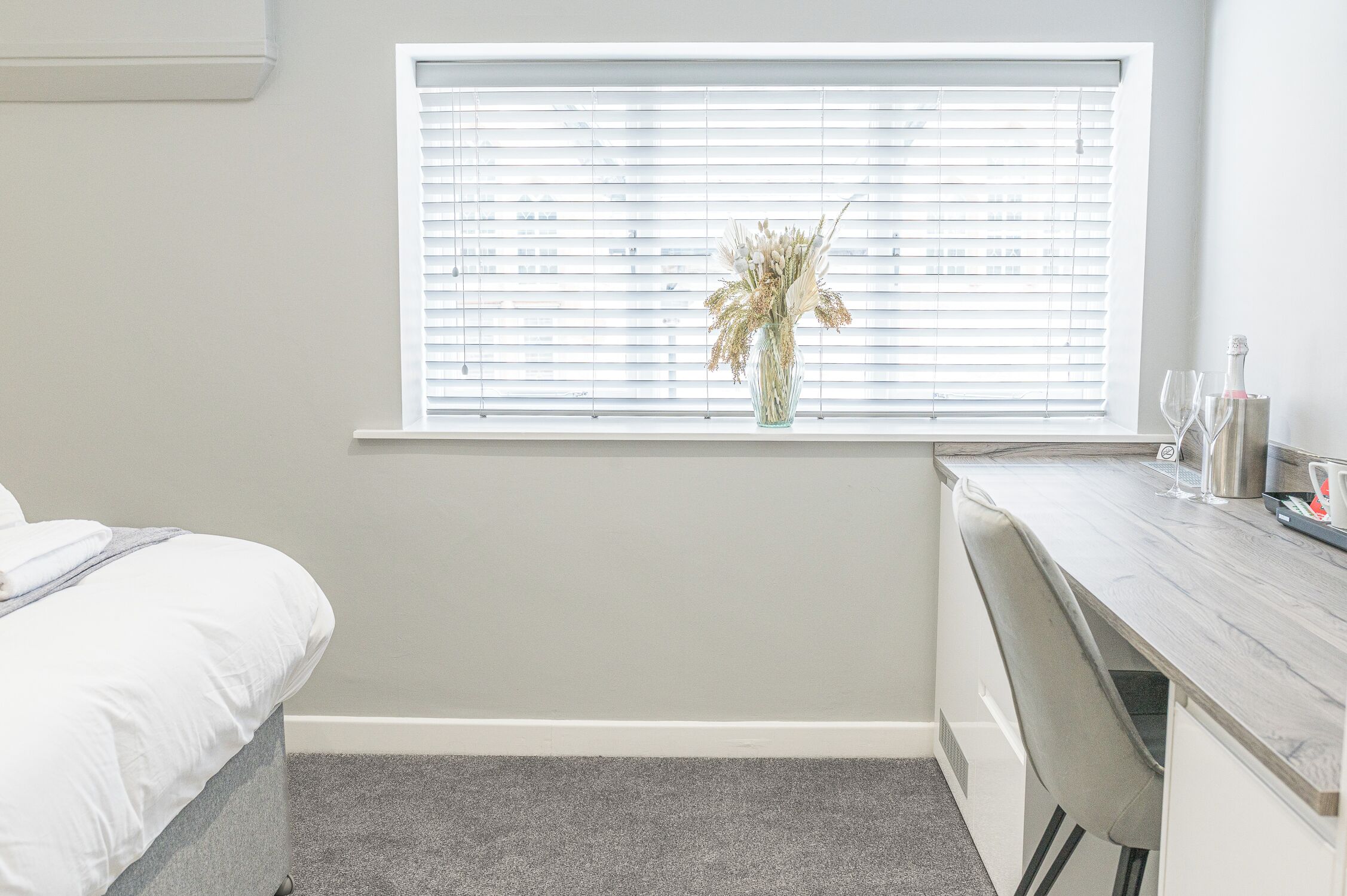 Ein Schlafzimmer mit Bett, Schreibtisch und einem Fenster mit Jalousien.