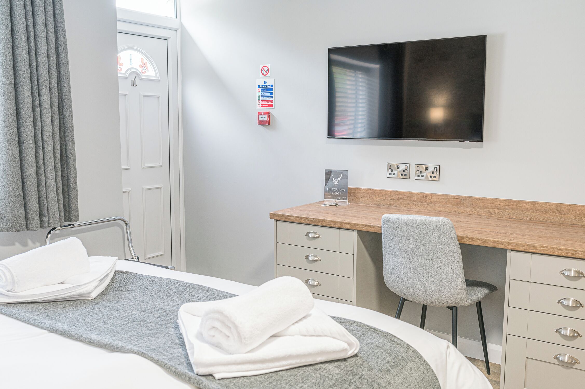 A hotel room with a bed, a desk, a chair, a TV, and a door.