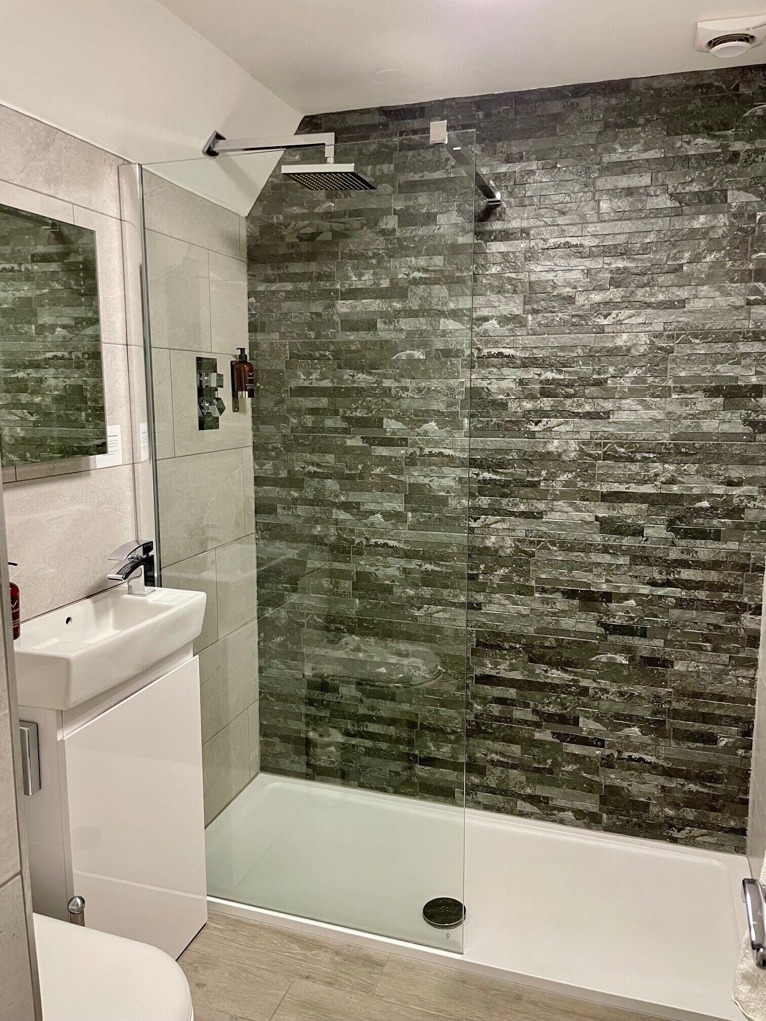 A modern bathroom with a glass-enclosed shower, a white sink, and a large mirror.