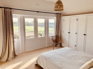 Relax in this serene bedroom with a large bed, wicker chair, and ample storage space.