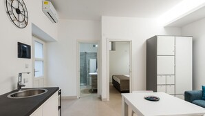 Une cuisine moderne équipée d’un évier, un coin repas avec une table et des chaises, et une chambre avec un lit et une armoire.