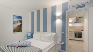 Ein Schlafzimmer mit Bett, Nachttisch, Stuhl, einem Bild an der Wand und Blick zur Küche.